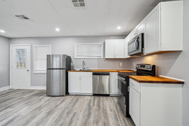 kitchen with butcher block countertops, white cabinets, appliances with stainless steel finishes, and light hardwood / wood-style flooring