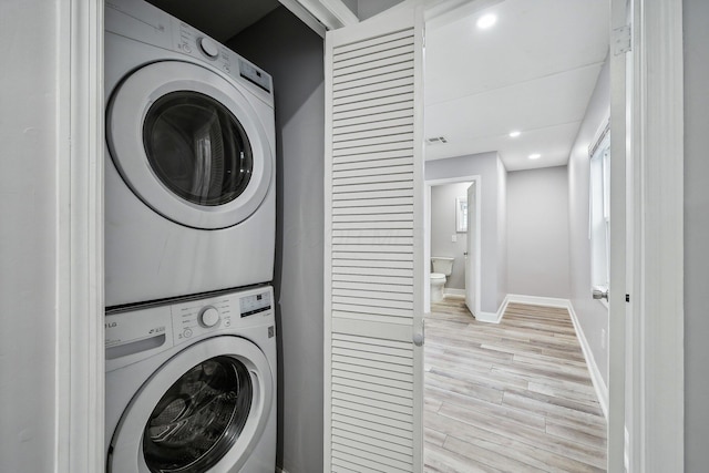 laundry room with light hardwood / wood-style floors and stacked washer / dryer