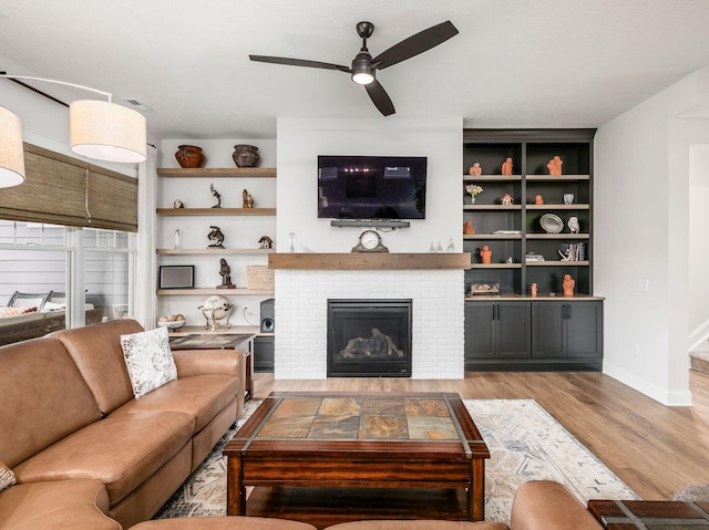 living room with a fireplace, light wood-type flooring, and ceiling fan