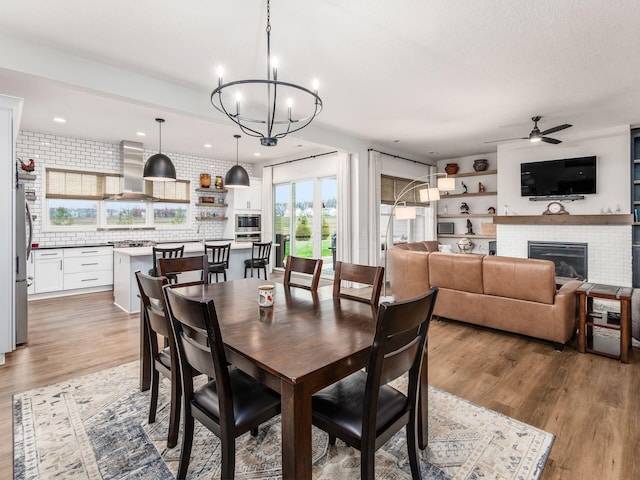 dining area featuring ceiling fan with notable chandelier, light wood-type flooring, and a fireplace