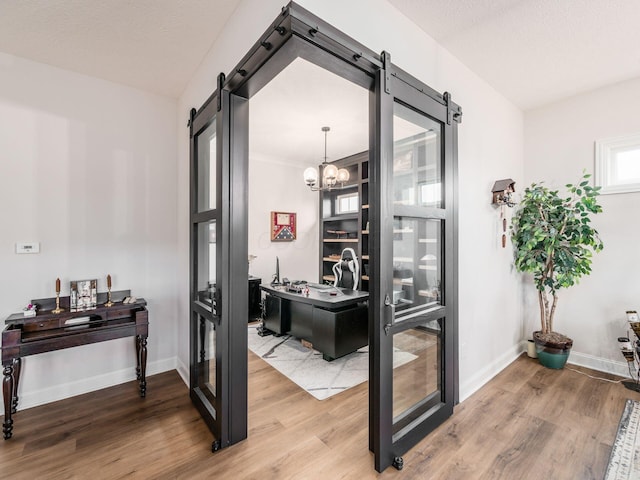 office featuring a notable chandelier, wood-type flooring, and a barn door