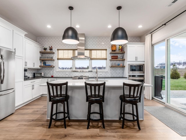 kitchen with decorative light fixtures, white cabinetry, exhaust hood, and appliances with stainless steel finishes