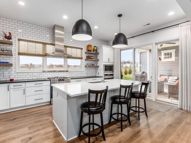 kitchen with stainless steel appliances, wall chimney range hood, white cabinets, and sink