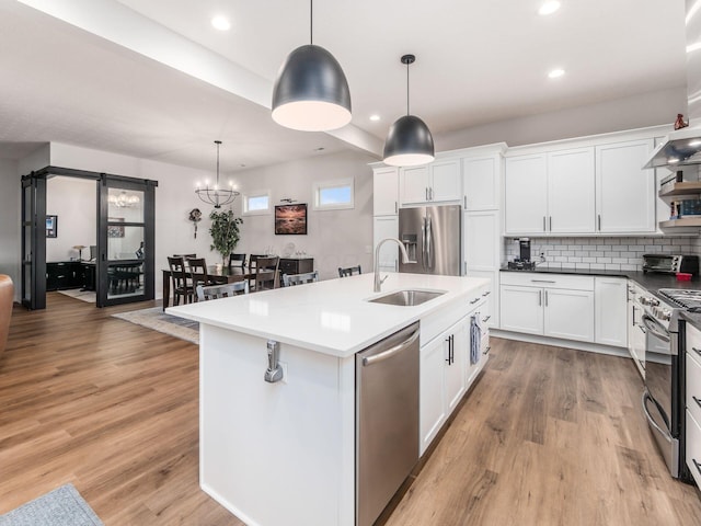 kitchen featuring pendant lighting, an island with sink, backsplash, white cabinetry, and appliances with stainless steel finishes