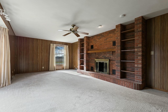 unfurnished living room with wooden walls, ceiling fan, light colored carpet, and a brick fireplace