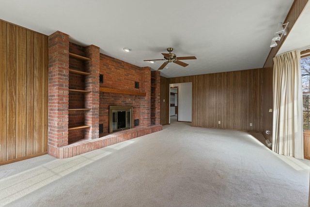 unfurnished living room featuring a fireplace, carpet, ceiling fan, and wood walls