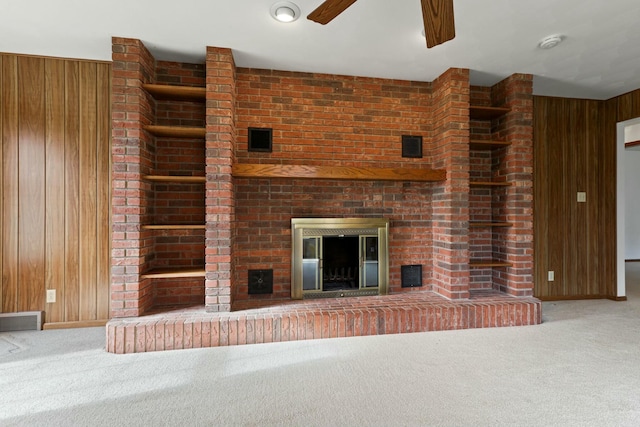 unfurnished living room featuring a fireplace, carpet flooring, ceiling fan, and wooden walls