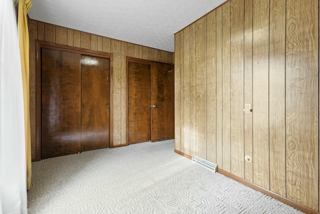 unfurnished bedroom with light colored carpet, multiple closets, and wood walls