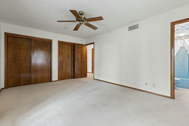 unfurnished bedroom with ceiling fan, multiple closets, light carpet, and ensuite bath