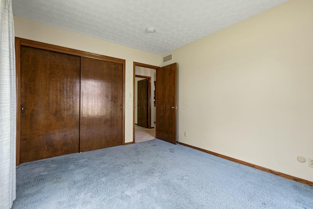 unfurnished bedroom featuring light colored carpet, a textured ceiling, and a closet