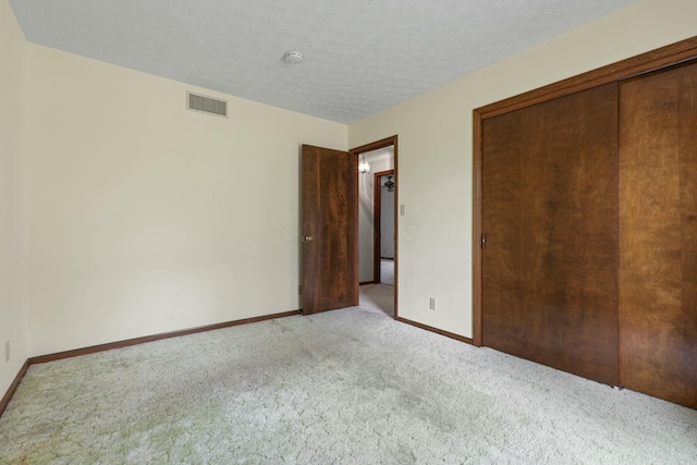 unfurnished bedroom with a textured ceiling, light colored carpet, and a closet