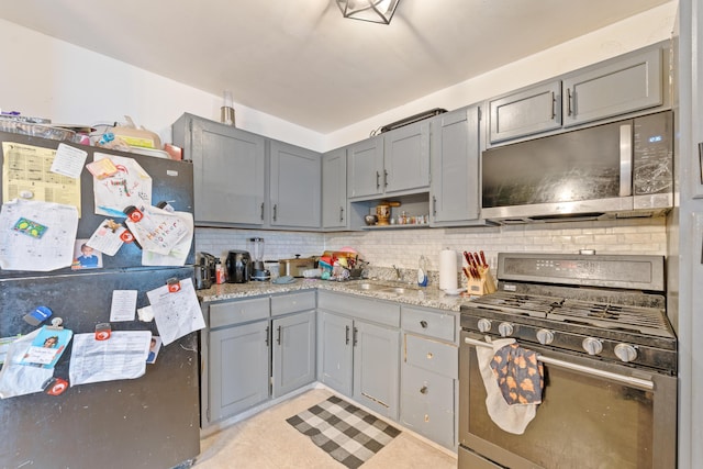 kitchen featuring backsplash, sink, gray cabinets, light stone counters, and stainless steel appliances