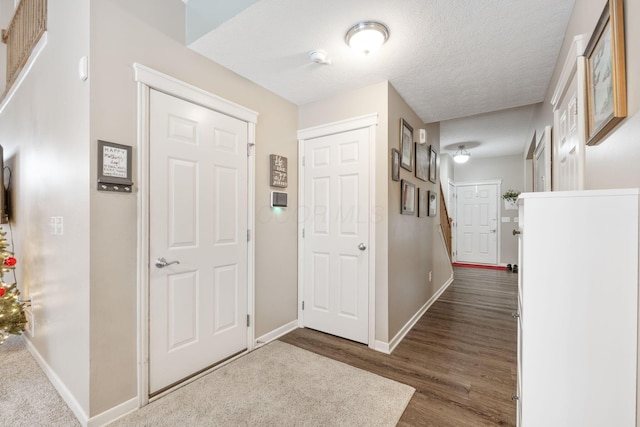 foyer entrance with a textured ceiling, baseboards, and wood finished floors