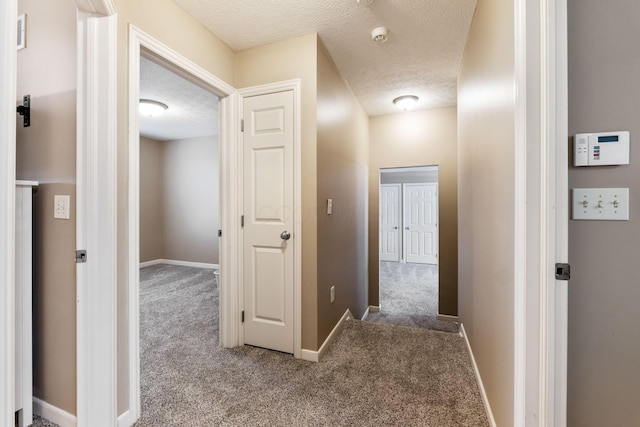 hall featuring carpet floors, baseboards, and a textured ceiling