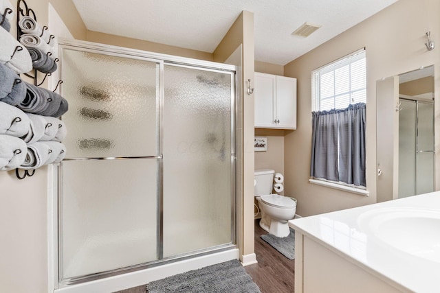 bathroom with a stall shower, visible vents, toilet, wood finished floors, and vanity