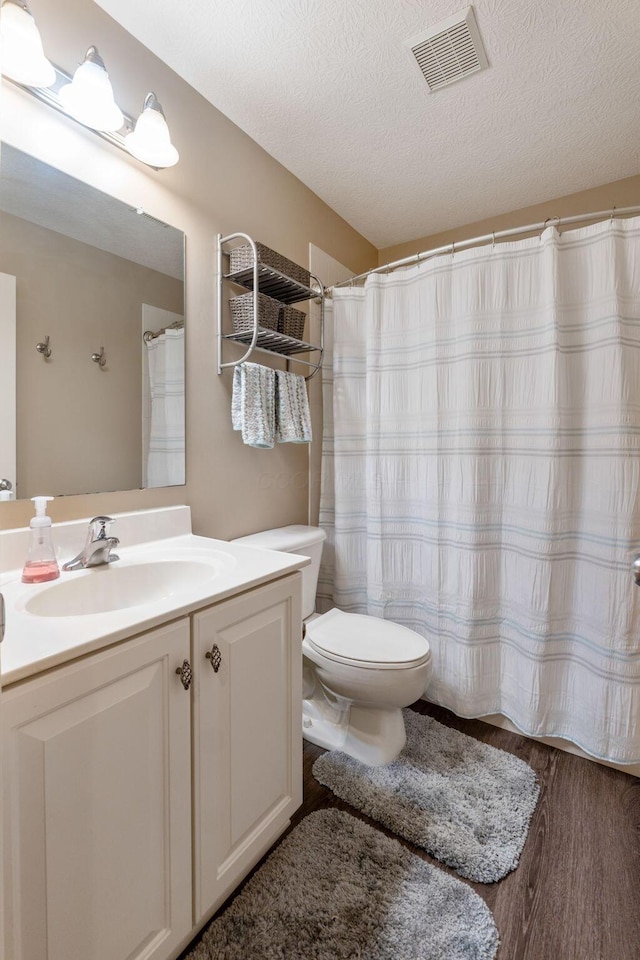 bathroom featuring visible vents, toilet, vanity, a textured ceiling, and wood finished floors