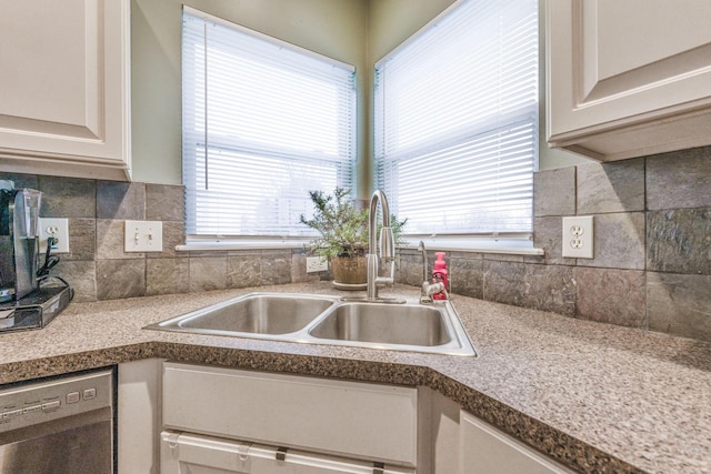 kitchen with light countertops, backsplash, white cabinetry, a sink, and dishwasher