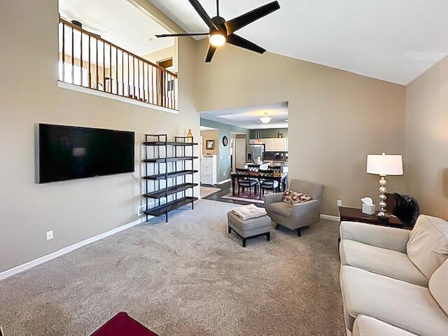 living room featuring carpet floors, ceiling fan, high vaulted ceiling, and baseboards