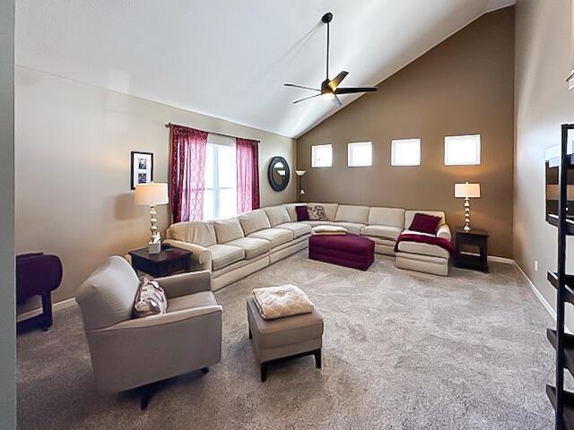 carpeted living area with a ceiling fan, high vaulted ceiling, and baseboards