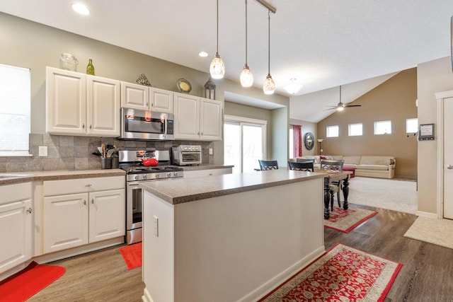 kitchen with stainless steel appliances, a kitchen island, white cabinetry, open floor plan, and hanging light fixtures