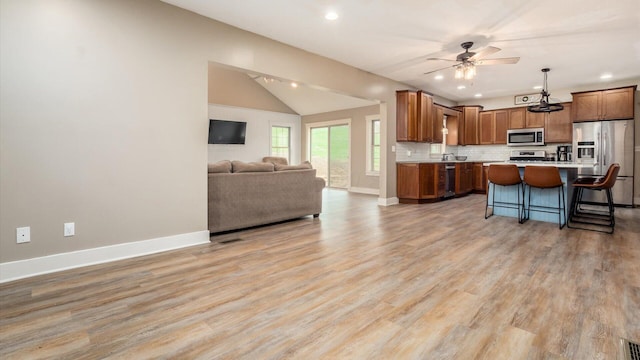 kitchen with appliances with stainless steel finishes, a kitchen breakfast bar, a center island, light hardwood / wood-style floors, and hanging light fixtures