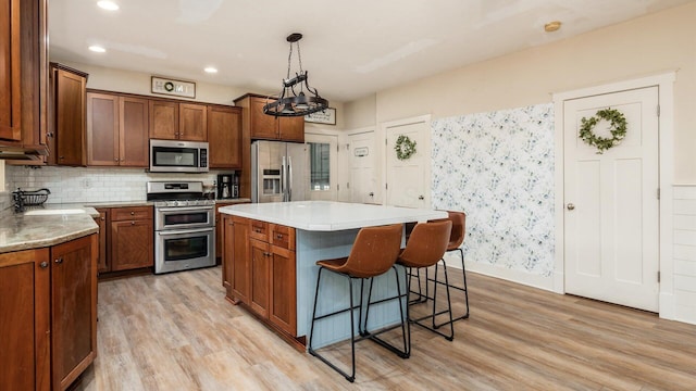 kitchen with appliances with stainless steel finishes, light wood-type flooring, backsplash, decorative light fixtures, and a center island