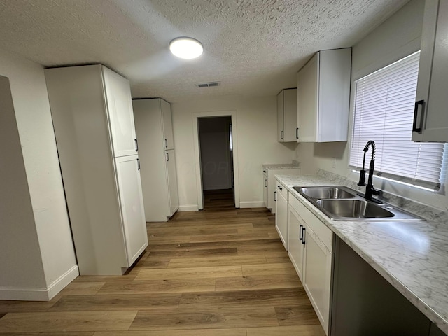 kitchen with a textured ceiling, light hardwood / wood-style floors, white cabinetry, and sink