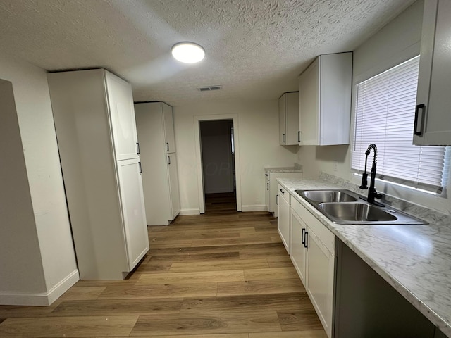 kitchen with a textured ceiling, white cabinets, light wood-type flooring, and sink