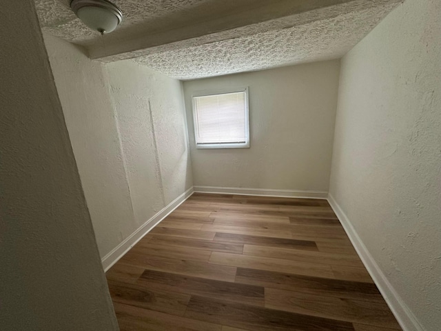 empty room featuring beamed ceiling, wood-type flooring, and a textured ceiling