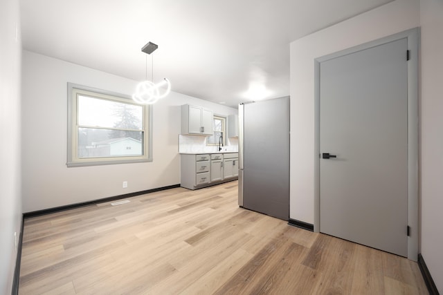 interior space with sink, tasteful backsplash, pendant lighting, gray cabinets, and light wood-type flooring