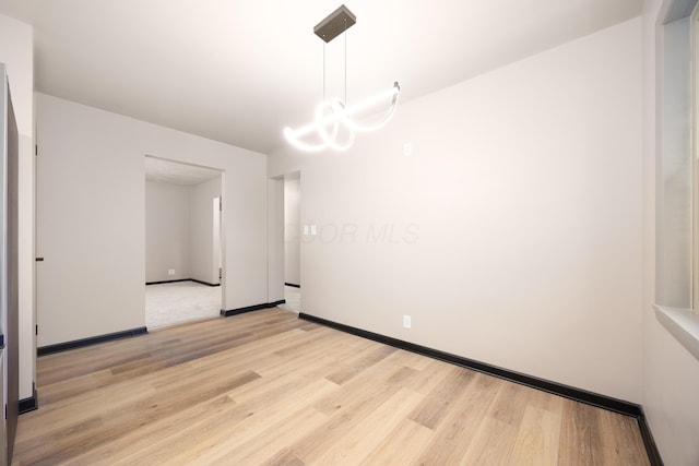 empty room featuring a chandelier and light wood-type flooring