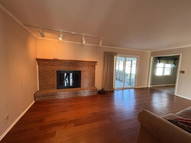 unfurnished living room featuring dark hardwood / wood-style floors, ornamental molding, a fireplace, and track lighting