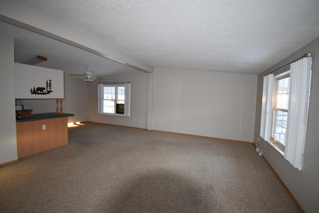 unfurnished living room featuring a textured ceiling, vaulted ceiling, plenty of natural light, carpet flooring, and ceiling fan