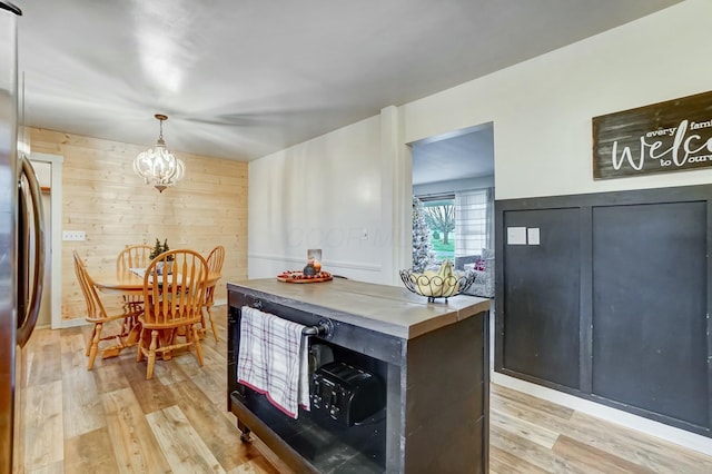 kitchen featuring fridge, light hardwood / wood-style flooring, a chandelier, hanging light fixtures, and wood walls