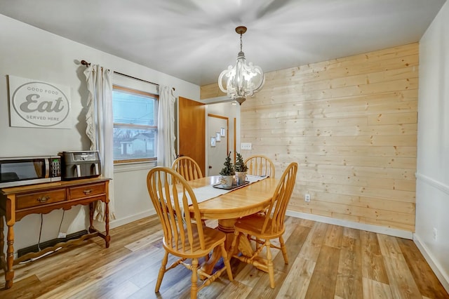 dining room with light hardwood / wood-style floors, an inviting chandelier, and wood walls