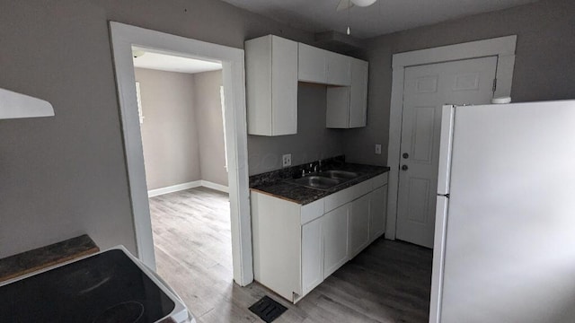 kitchen with white cabinets, white refrigerator, light hardwood / wood-style floors, and sink