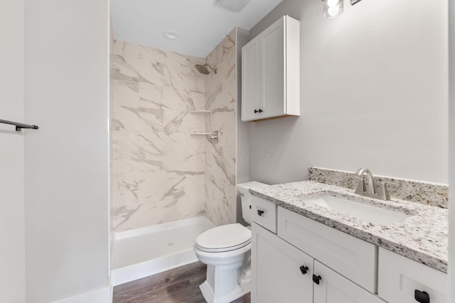 bathroom featuring a tile shower, vanity, a textured ceiling, hardwood / wood-style flooring, and toilet