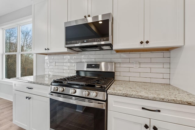 kitchen with light stone countertops, white cabinetry, stainless steel appliances, and light wood-type flooring