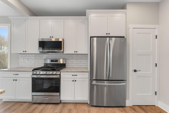 kitchen with backsplash, white cabinets, appliances with stainless steel finishes, light hardwood / wood-style floors, and light stone counters