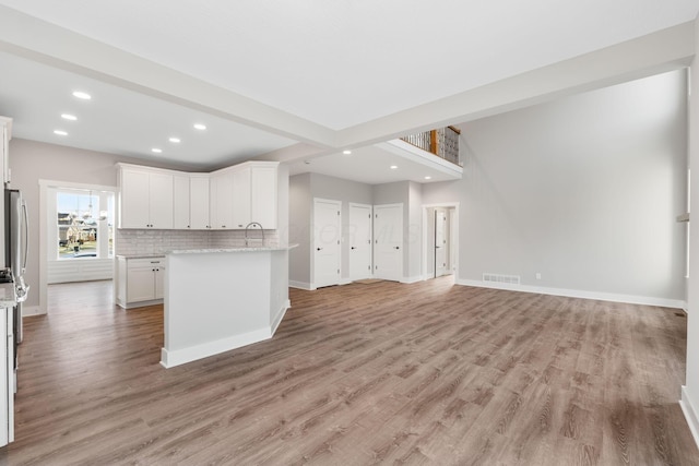 kitchen featuring light stone countertops, tasteful backsplash, beam ceiling, light hardwood / wood-style floors, and white cabinetry