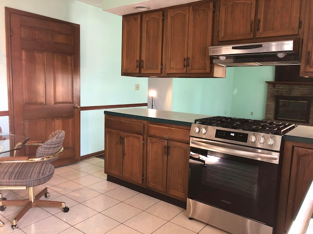 kitchen with light tile patterned floors, high end stove, a brick fireplace, and range hood