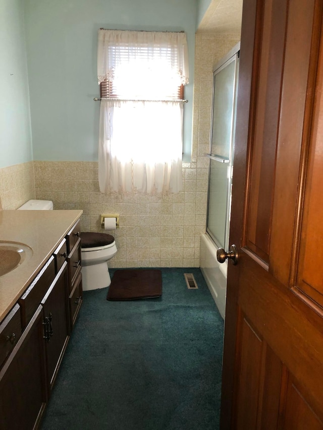 full bathroom featuring toilet, combined bath / shower with glass door, tile walls, and vanity