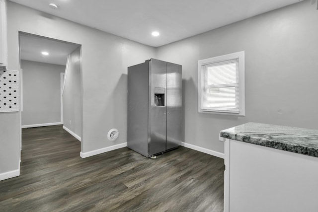 kitchen featuring stone counters, dark wood-style flooring, stainless steel fridge with ice dispenser, white cabinets, and baseboards