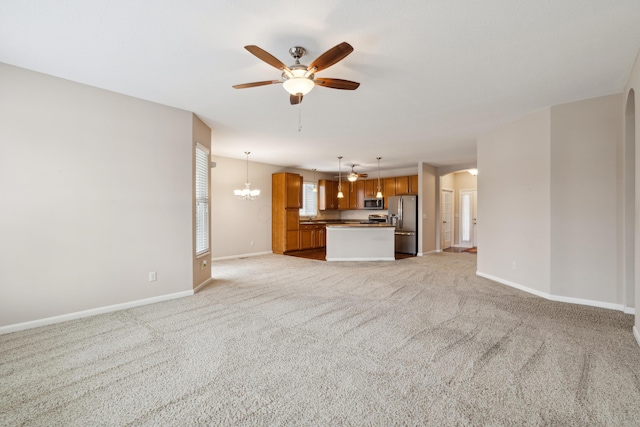 unfurnished living room with ceiling fan with notable chandelier and light colored carpet