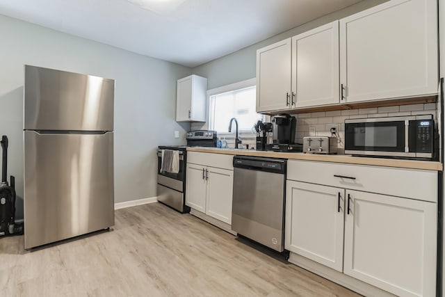 kitchen with appliances with stainless steel finishes, light wood-type flooring, white cabinetry, and backsplash