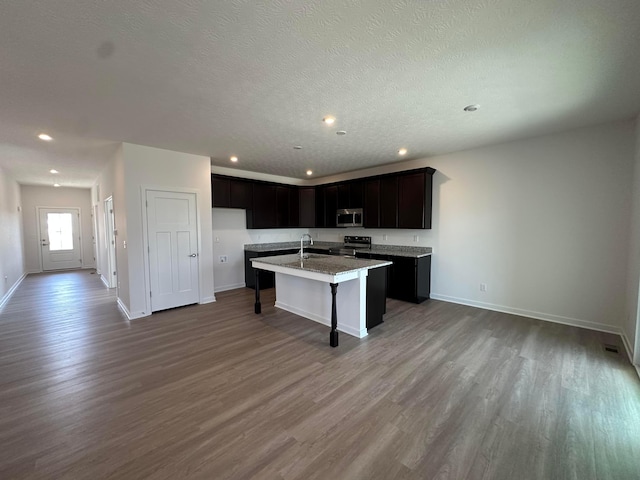 kitchen featuring an island with sink, a sink, wood finished floors, a kitchen bar, and appliances with stainless steel finishes