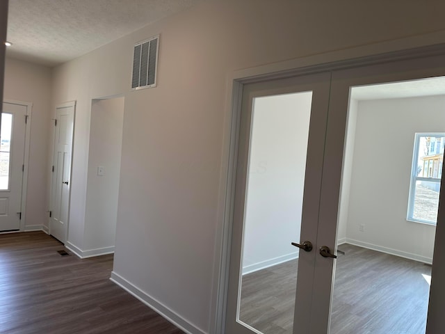 hallway with dark wood-type flooring, baseboards, a textured ceiling, and visible vents
