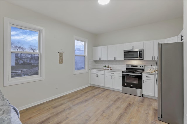 kitchen with stainless steel appliances, tasteful backsplash, light stone counters, light hardwood / wood-style flooring, and white cabinets