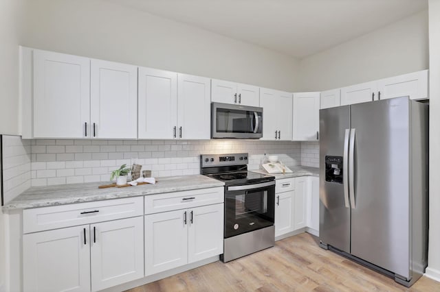 kitchen with tasteful backsplash, light stone counters, white cabinets, and stainless steel appliances