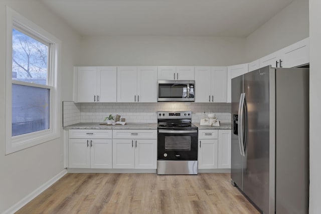 kitchen with light stone countertops, stainless steel appliances, backsplash, light hardwood / wood-style floors, and white cabinets